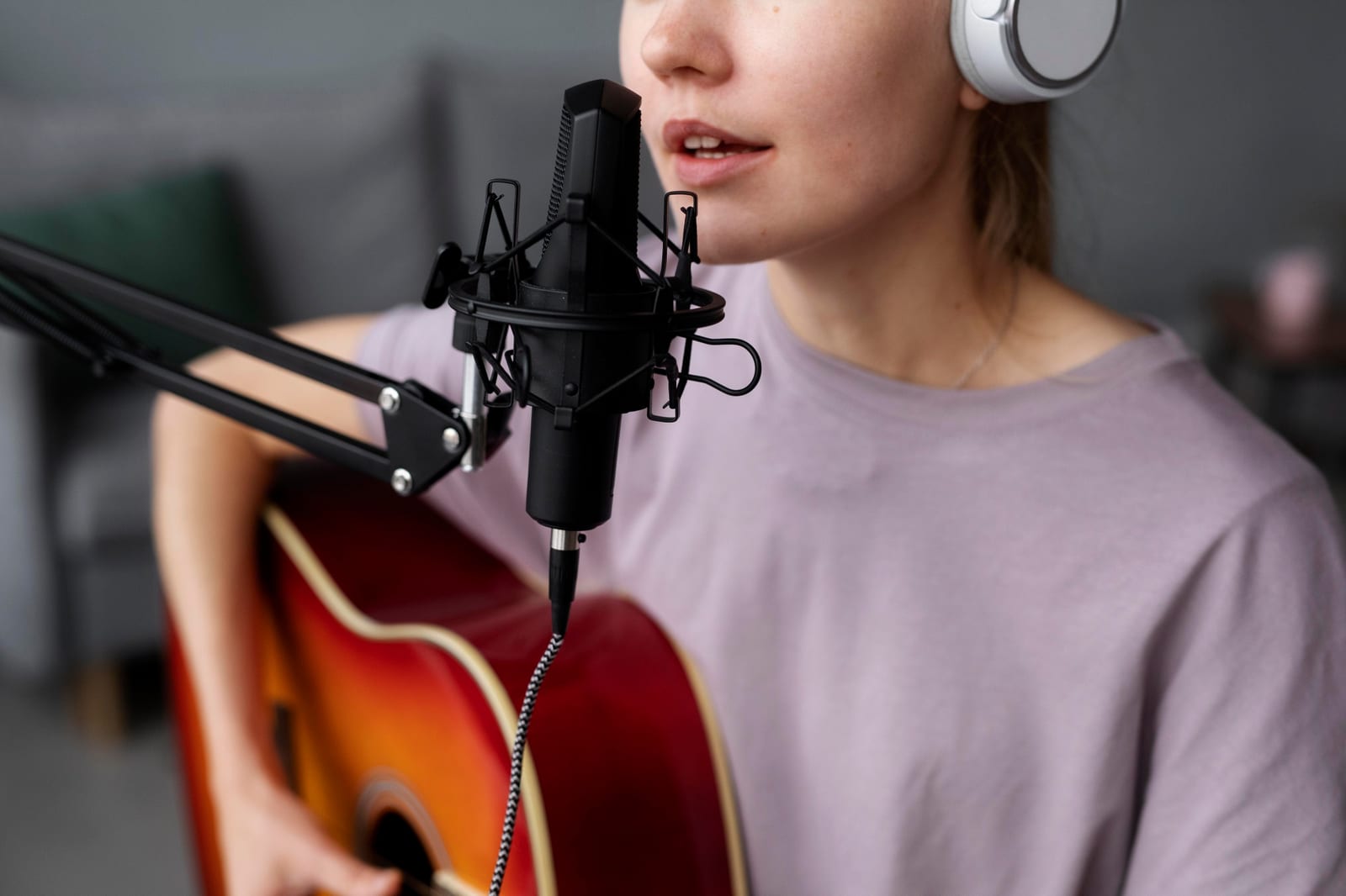 Mulher com fones de ouvido canta ao microfone condensador enquanto toca violão.