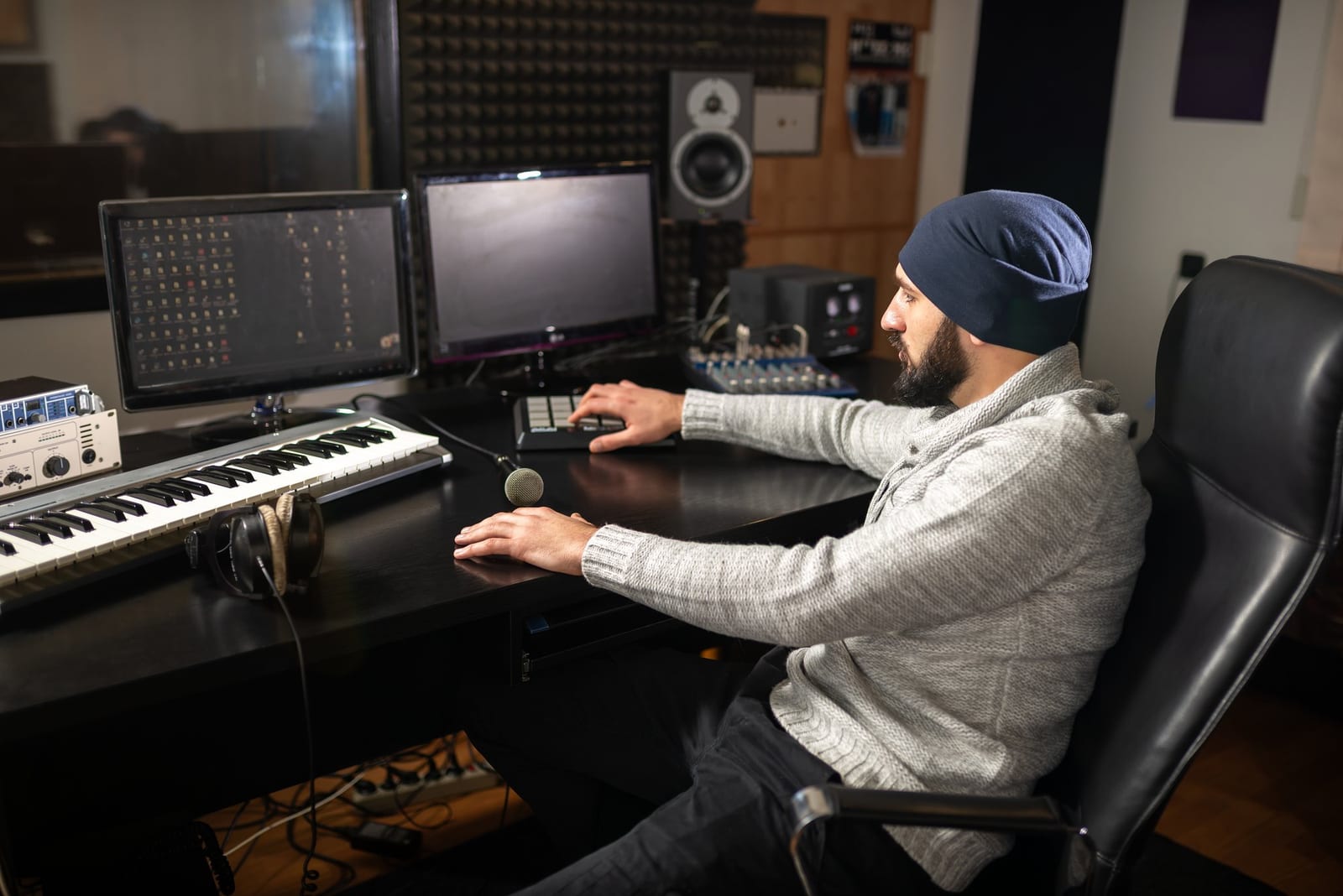 Produtor usa controlador e teclado MIDI diante de monitores em uma sala de gravação.